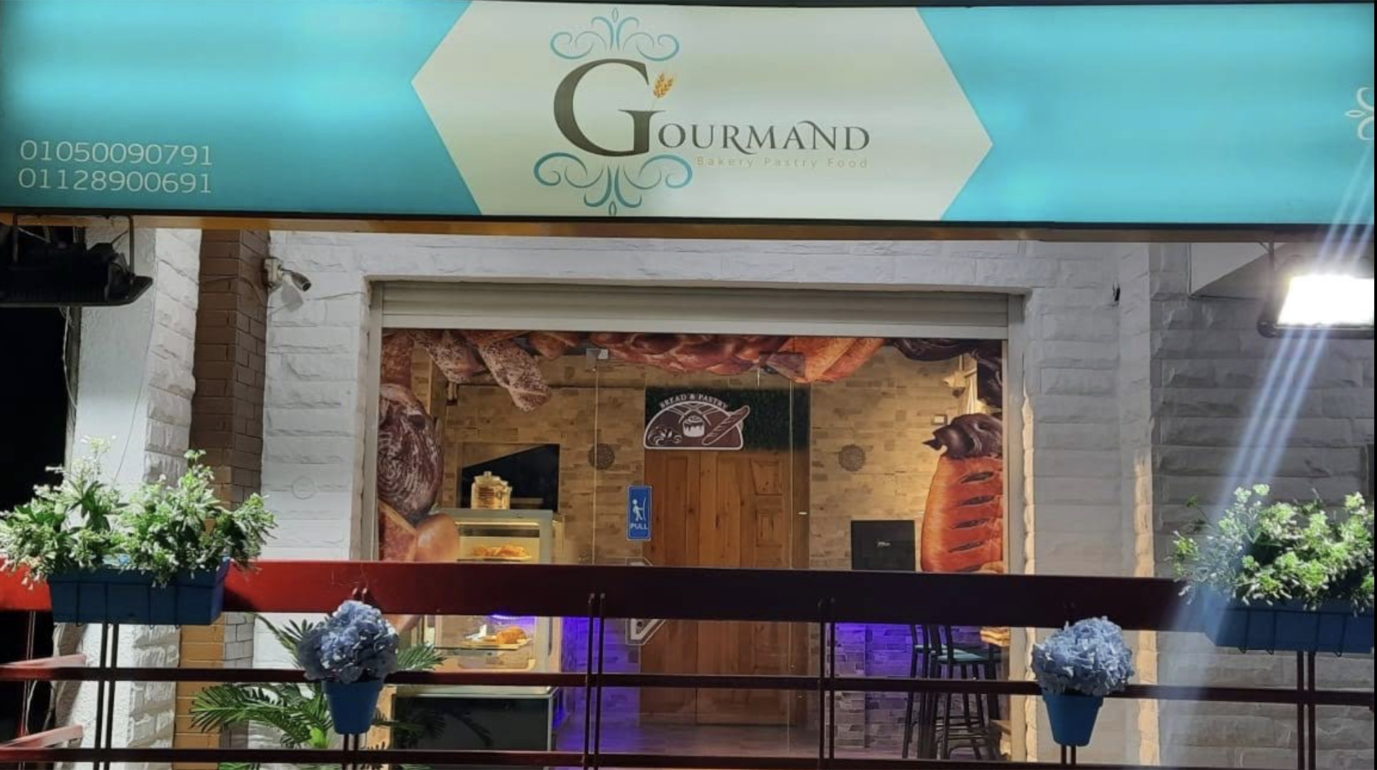 The Gourmand storefront in Nasr City, Cairo. Teal awning with gold serif wordmark, white brick walls.